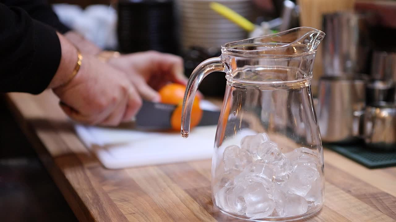 Barman che taglia un'arancia mentre prepara una limonata tropicale nella brocca
