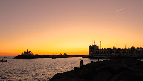 fishermen on pier and coast during orange sunset casting fishing line on the open sea in the background is the city and harbor of sunset grand canary island valley 4k slow motion capture at 60fps