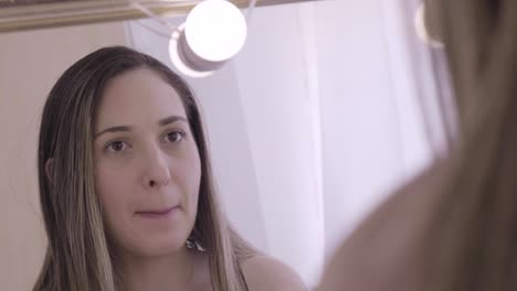 close up of young woman putting lipstick on in front of the mirror