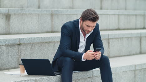 Hombre-De-Negocios-Enviando-Mensajes-De-Texto-Por-Teléfono-Celular-En-La-Calle.-Profesional-Trabajando-En-Teléfono-Inteligente