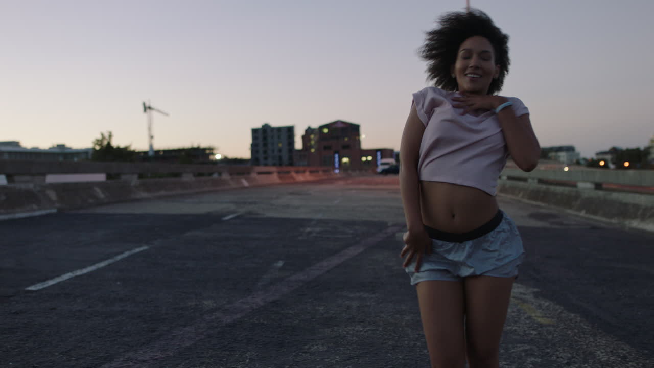 donna ballerina di strada di razza mista donna con afro funky che esegue movimenti freestyle hip hop godendosi l'espressione della danza moderna in città al tramonto