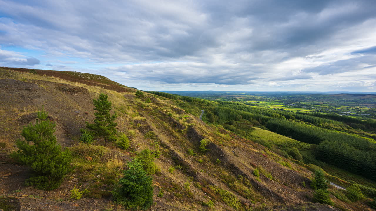 panorama motion timelapse de paisaje rural con árboles de coníferas en la ladera y bosques en la distancia durante un día nublado y soleado visto desde arriba lough mealagh en el condado de roscommon en irlanda