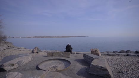 person in toronto trillium park with hijab sitting near lake in bright yellow jacket during day