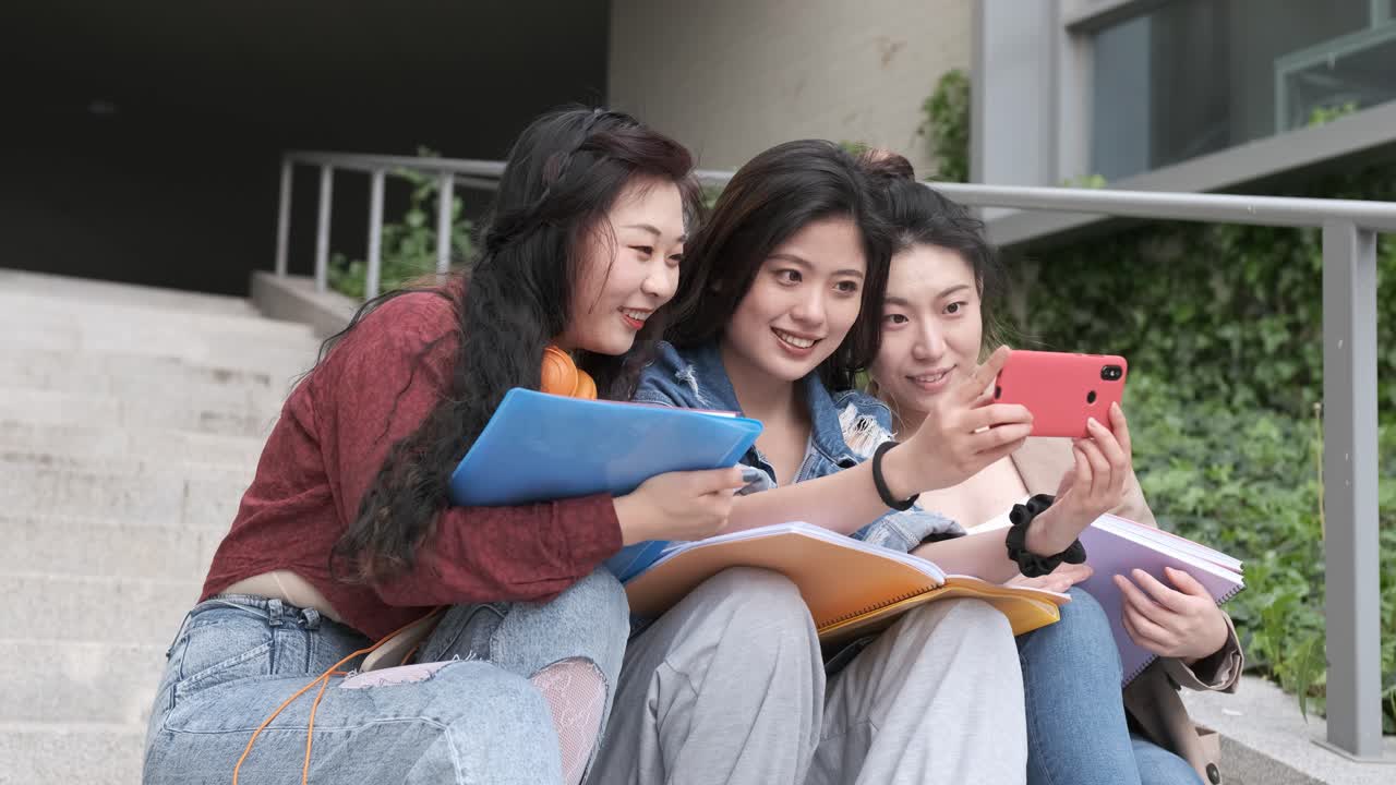 Asian college students taking a selfie with a mobile phone outside the university campus. Education concept.
