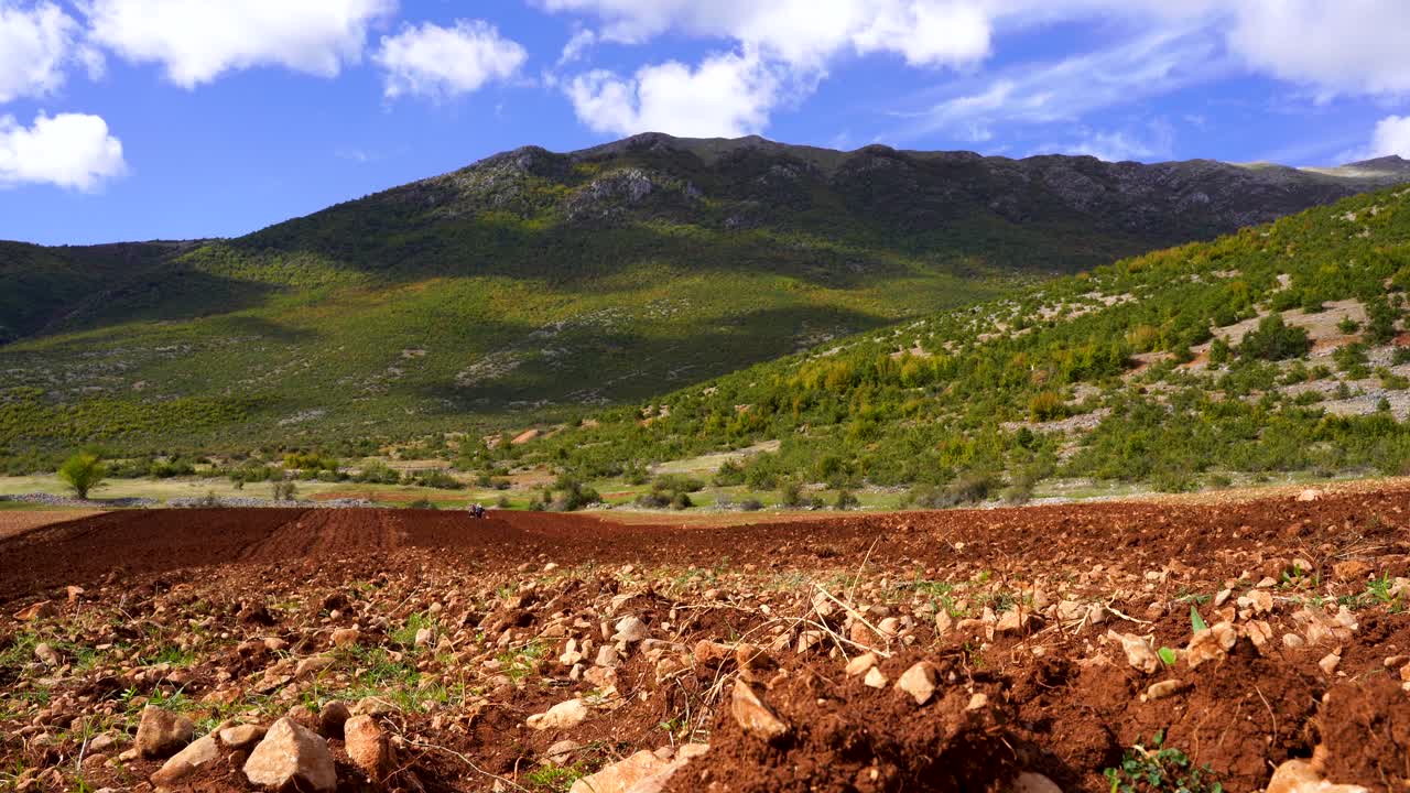 tierra cultivada con tierra roja y montañas verdes en el fondo bajo un cielo nublado en los balcanes