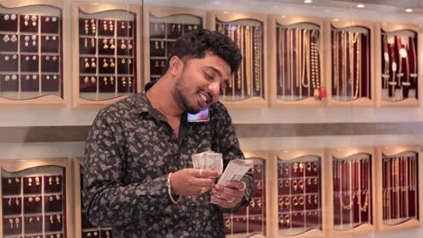 young man busy on mobile while counting money at gold jewelry showroom - concept of small business owners, young owner or entrepreneur