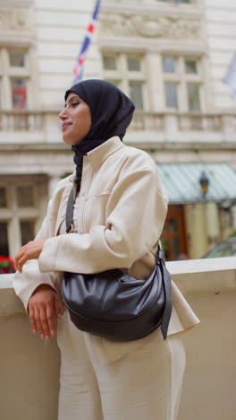 vertical video portrait of smiling muslim businesswoman wearing hijab and modern business suit standing outside city office buildings 4