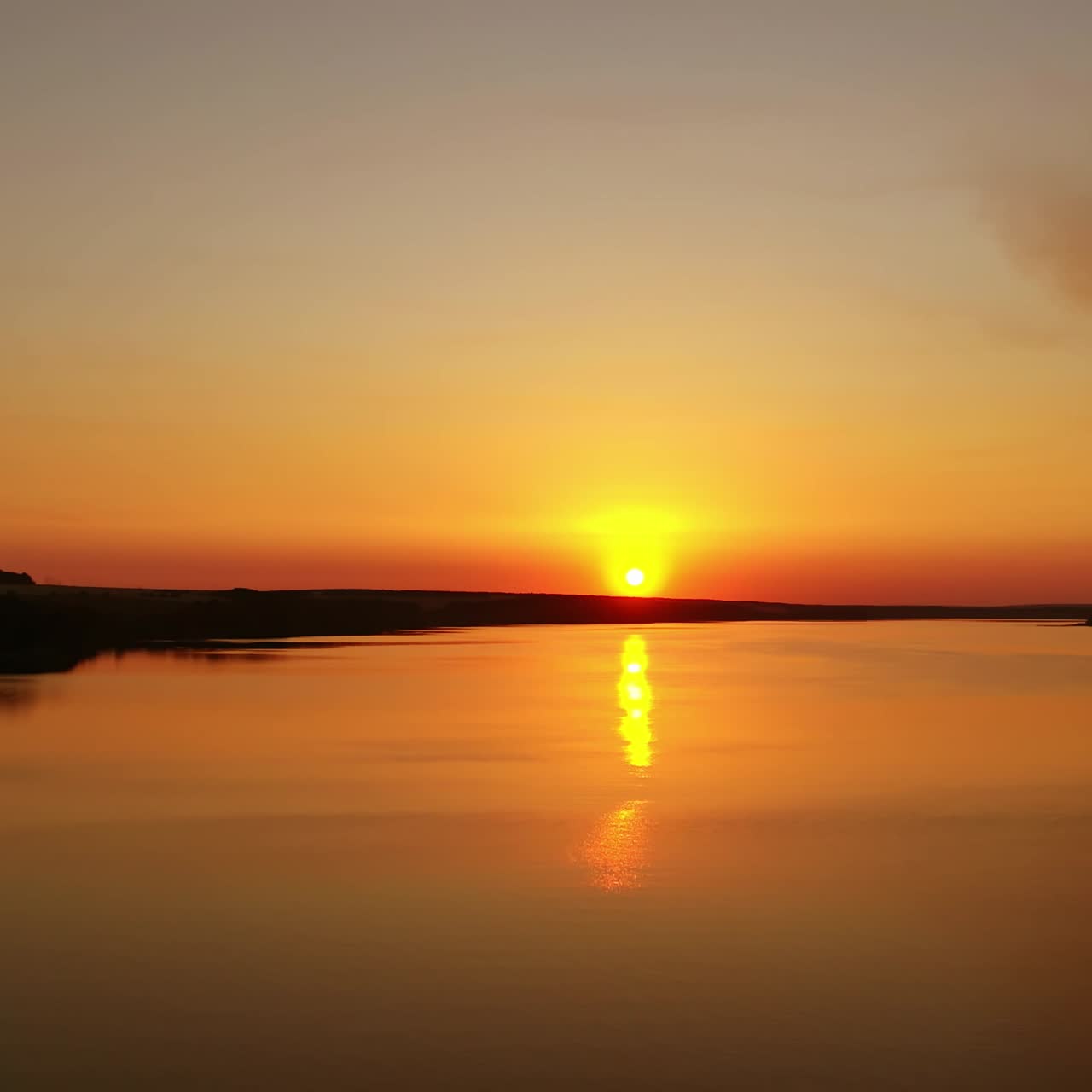 Amazing sunset over the water. Orange background from the setting sun. Golden path reflects on river in the evening.