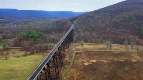 imagens de vídeo de drone aéreo de um viaduto de ponte de trem passando por um vale nas montanhas appalachain durante o início da primavera em um dia nublado, cercado por montanhas e terras agrícolas