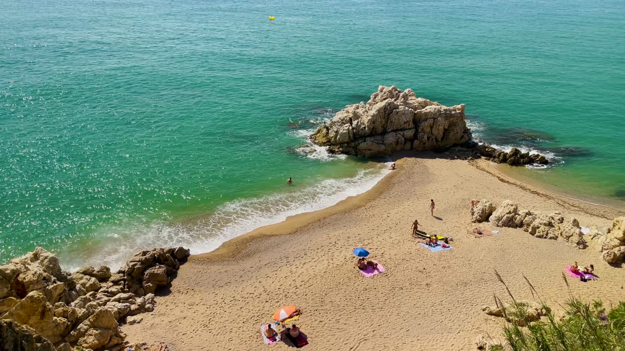costa brava cala roca grossa día soleado de verano mediterráneo europeo turismo paraíso playa vista aérea desde drone contraste con roca arena y árboles verdes