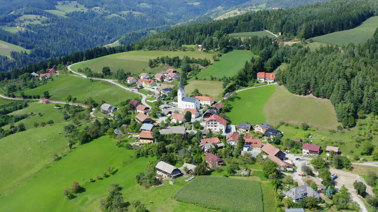 disparo aéreo en círculos sobre un pequeño pueblo con una iglesia en el medio en prevalje, eslovenia