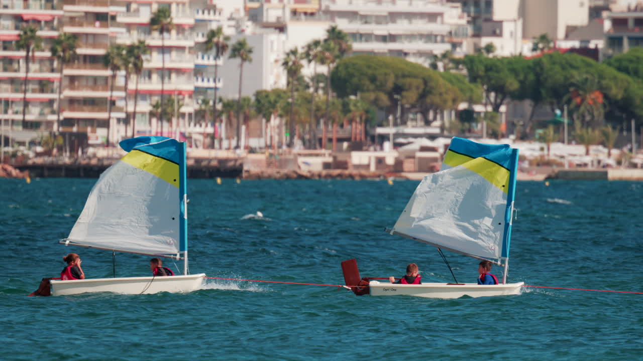Cannes, France - October 7, 2025: Children in small sailboats learning to navigate on the blue sea near a beach resort