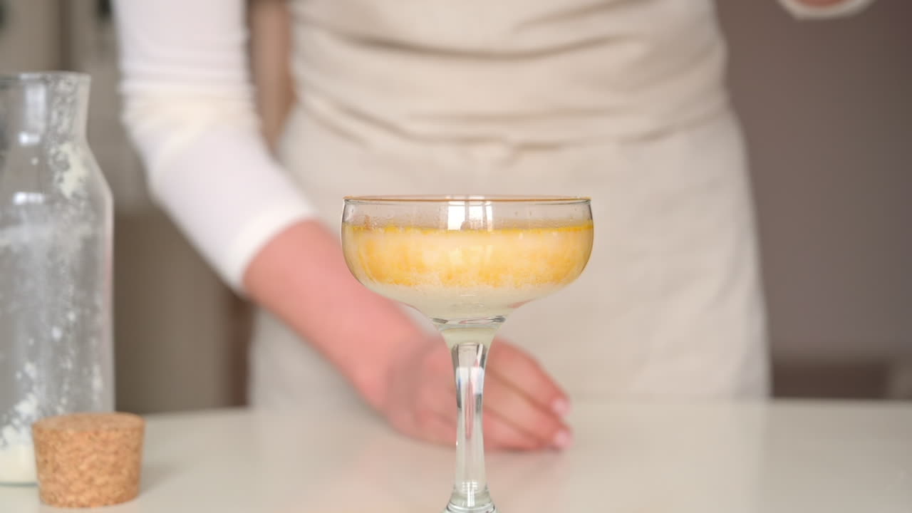 Donna con un grembiule che versa polvere gialla nel latte in un bicchiere da cocktail in cucina