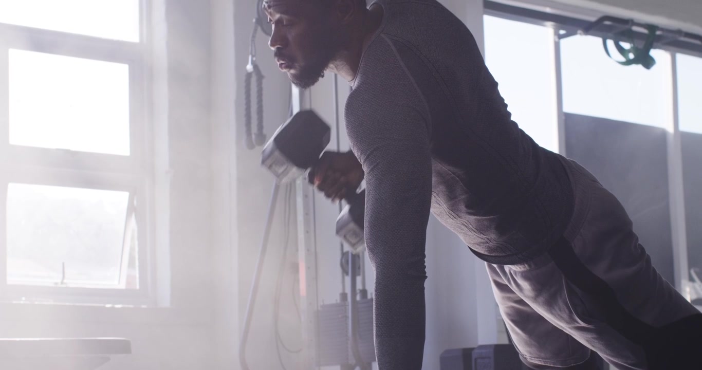 African American male gripping hex dumbbells on gym floor pushing rowing building strength