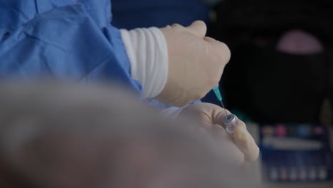 an elderly patient waits as a nurse prepares the covid vaccine