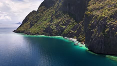 outrigger boats line the clear turquoise waters of talisay beach, surrounded by steep limestone cliffs and dense greenery on tapiutan island, philippines, in a peaceful tropical setting