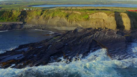 slow-motion waves crashing on the irish coast at the kilkee cliffs walk, illuminated by beautiful sunrise light