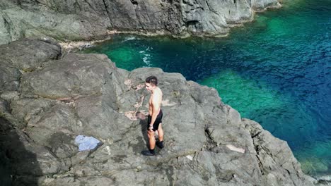 shirtless male tourist standing on tropical rock formation with clear, turquoise ocean waters in background