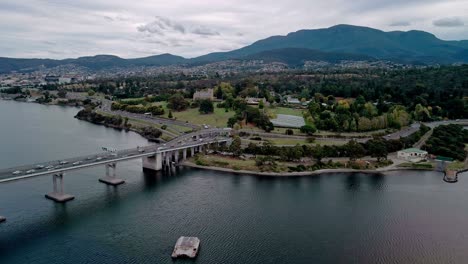 Drohnenansicht-Der-Stadtlandschaft-Und-Einer-Brücke-Mit-Bergen-Im-Hintergrund-Am-Abend