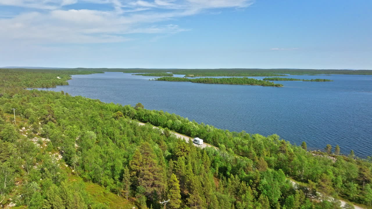 Drone tracking a Caravanette driving on a lakeside road, summer day in Lapland