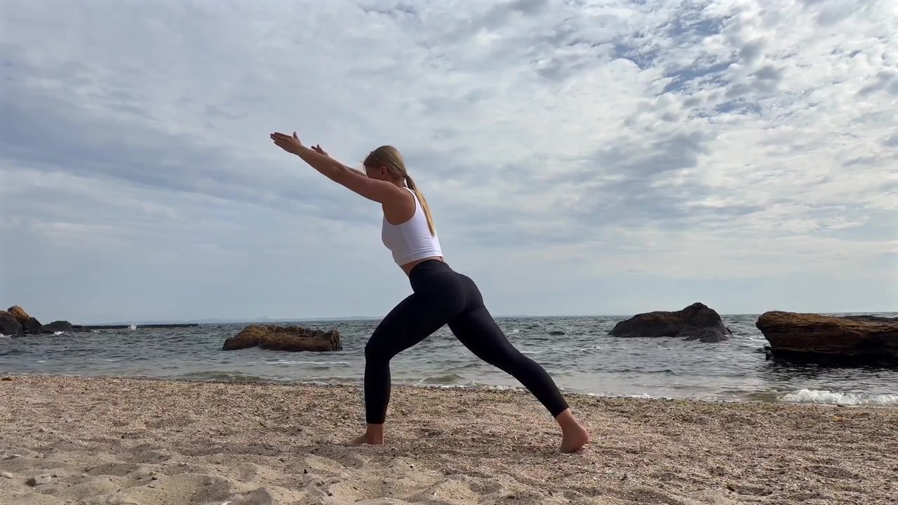 Giovane donna che pratica la posizione dell'affondo yoga sulla spiaggia