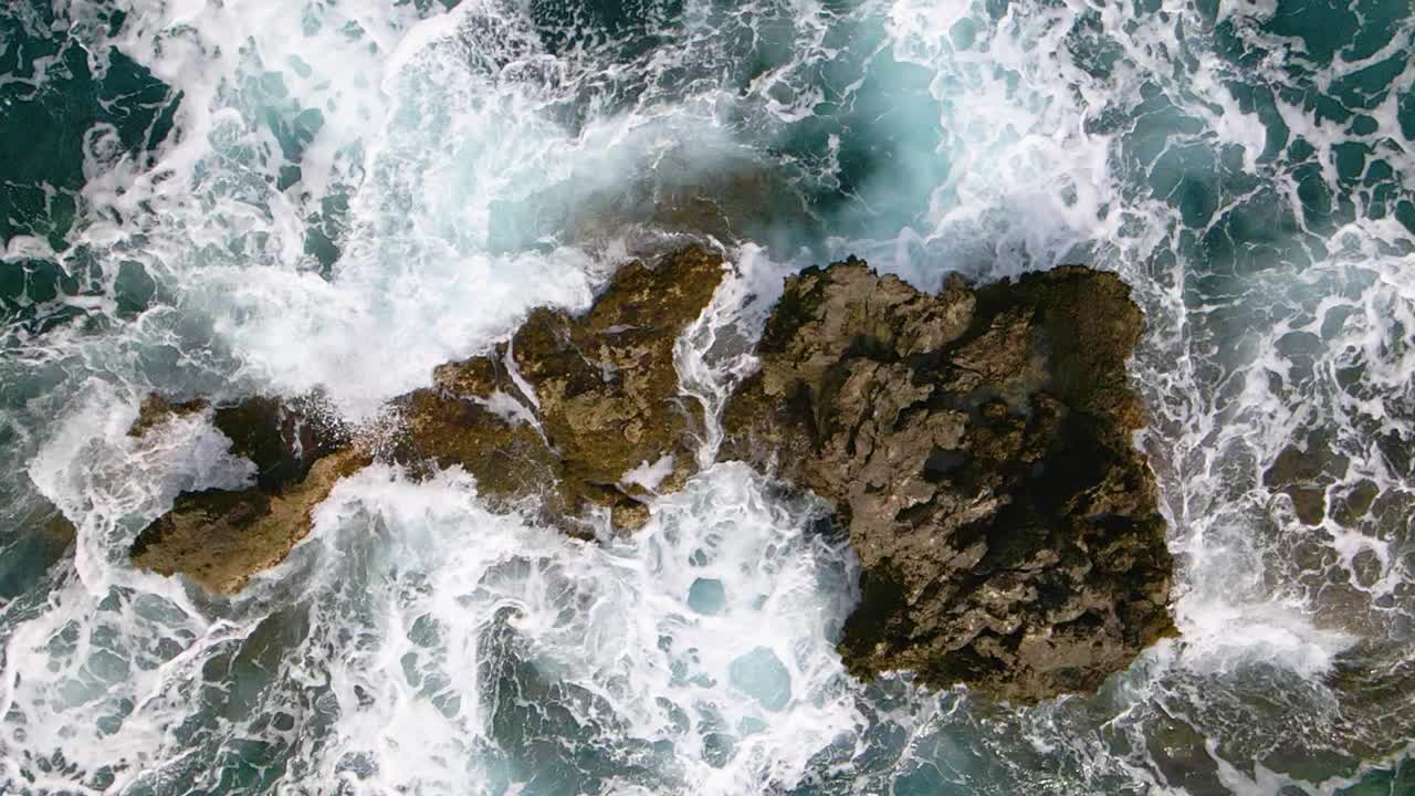 Vista aerea, dall'alto, ravvicinata dell'acqua del mare che lambisce le rocce in slow motion a 240fps