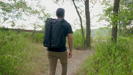 Hiker-with-modern-backpack-walking-through-summer-forest-towards-cliff-lookout-point