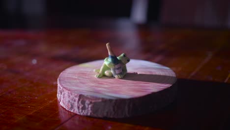 cute frog figurine made of ceramic holding miniature bottle of champagne on a wooden base, illuminated by glowing projector lights