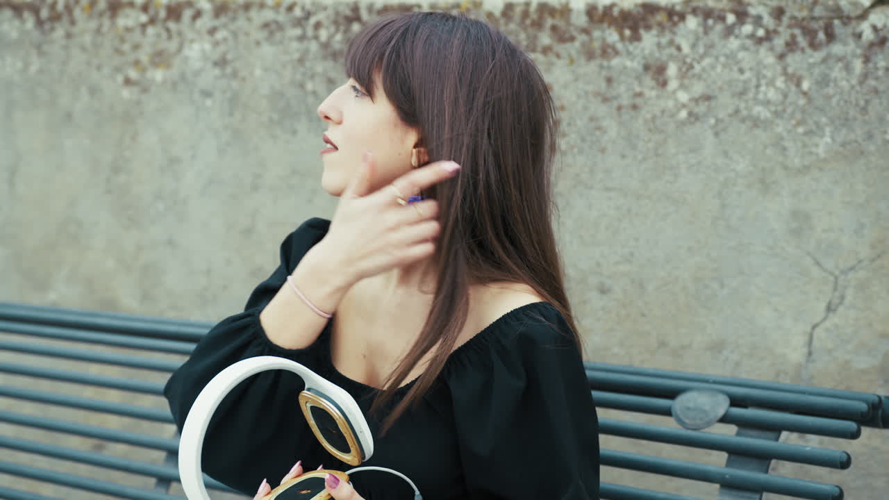 Woman Picking up Off The Headphones While Sitting On The Bench Outdoor