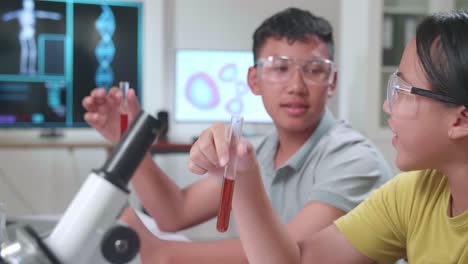 young asian boy and girl learning science experiment in laboratory at classroom. they are holding test tubes and talking together