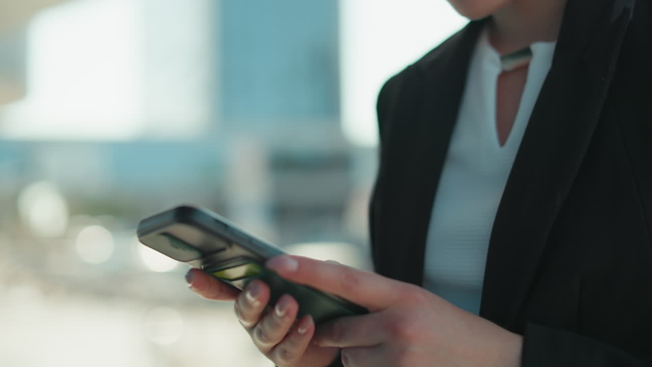 Close up of woman typing on phone with focus and precision, dressed in business attire, urban background with building blur effect and soft bokeh