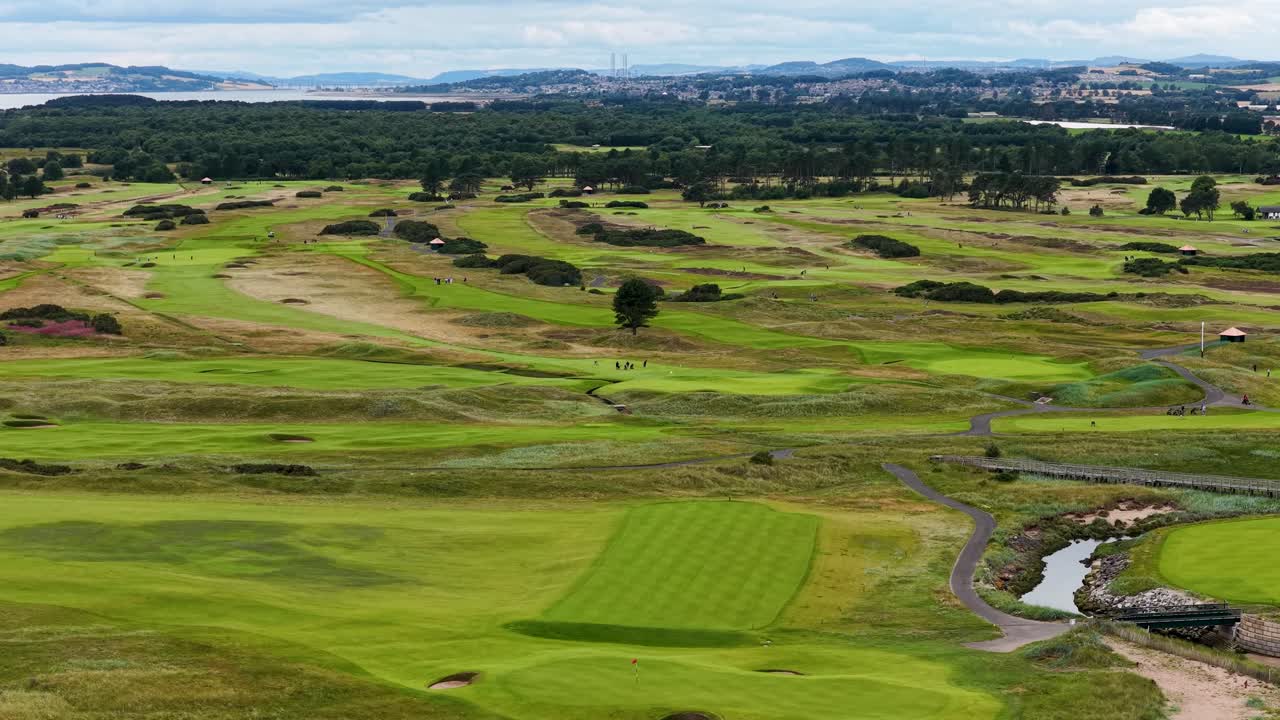 Sweeping aerial view of lush golf course fairways, greens, bunkers, and rolling Scottish landscape
