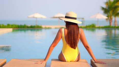 Una-Mujer-Atractiva-De-Espaldas-A-La-Cámara-Mientras-Mira-Al-Océano-Desde-La-Piscina-De-Un-Resort