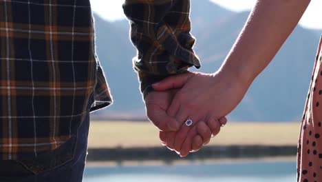 couple in love holding hands after getting engaged with engagement ring on finger looking out onto beautiful lake view