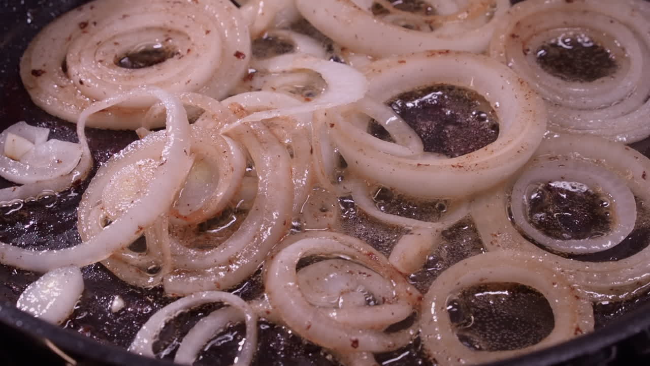 Close-up view: Rings of onion saute in hot oil in fry pan on stovetop