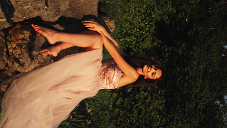 Young-Pretty-Woman-Wearing-Pink-Wedding-Dress,-Sitting-on-Rocks,-Forest-Background,-Barefoot,-Golden-Hour,-Bright-Natural-Sunlight,-Slow-Motion,-CInematic-Vertical