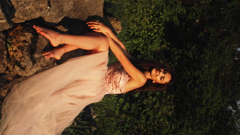 young pretty woman wearing pink wedding dress, sitting on rocks, forest background, barefoot, golden hour, bright natural sunlight, slow motion, cinematic vertical