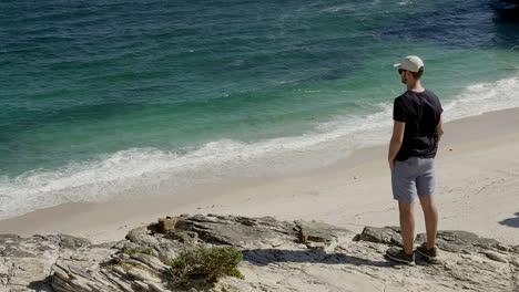 Man-standing-on-a-cliff-facing-the-ocean