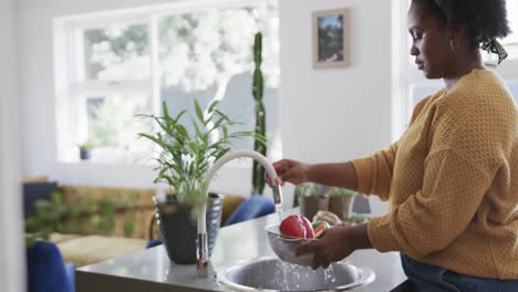 Profile-of-african-american-woman-rinsing-vegetables-in-kitchen-sink,-slow-motion