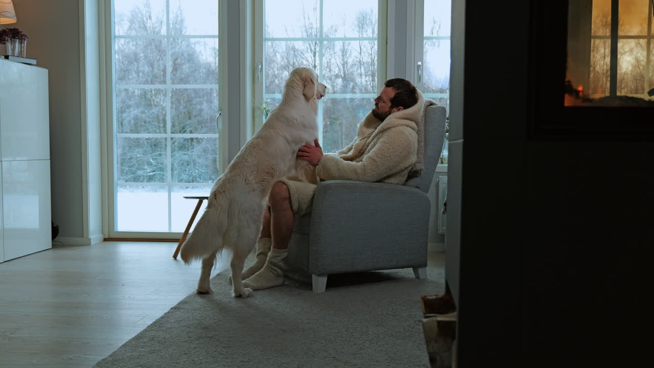 Man in cozy winter clothing sitting indoors, bonding with a large, affectionate dog