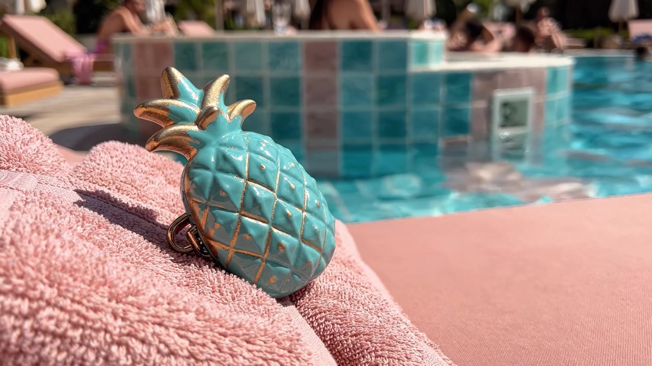 Eine bunte Ananas-Motivationsklammer, die auf einem weichen Handtuch am einladenden Poolrand liegt, ideal für sommerliche Entspannung und Urlaubsstimmung.