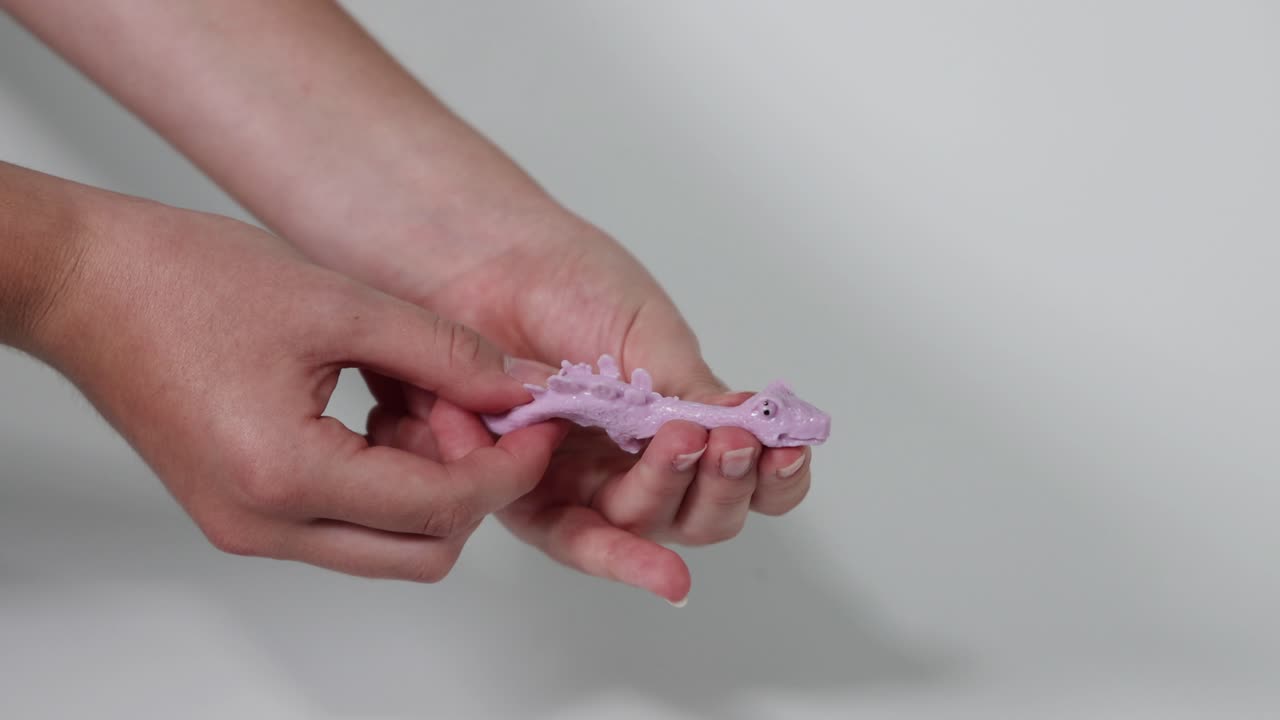 manos aplastando un juguete de dinosaurio púrpura repetidamente