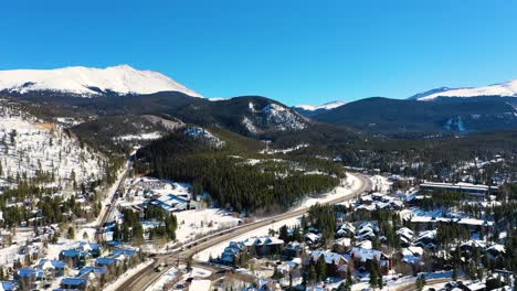 gorgeous breckenridge colorado mountain town with snow-covered houses and people driving on road through pine tree forest, aerial drone view