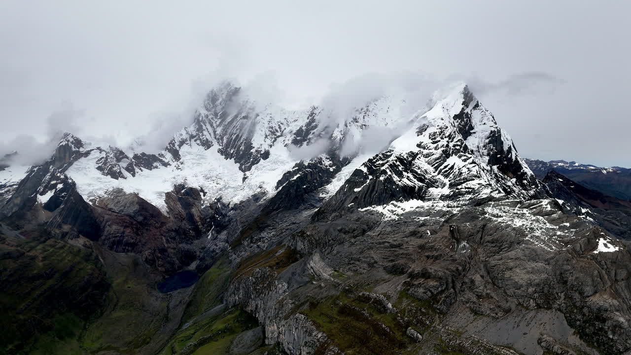 Cinematic aerial view of snowy Andes mountains in Peru with glaciers, rocky cliffs, and hidden blue alpine lake under misty clouds, dramatic landscape and natural travel destination