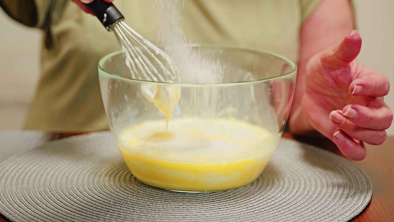 Slow motion close up, sugar falling into whisked eggs creating soft golden foam