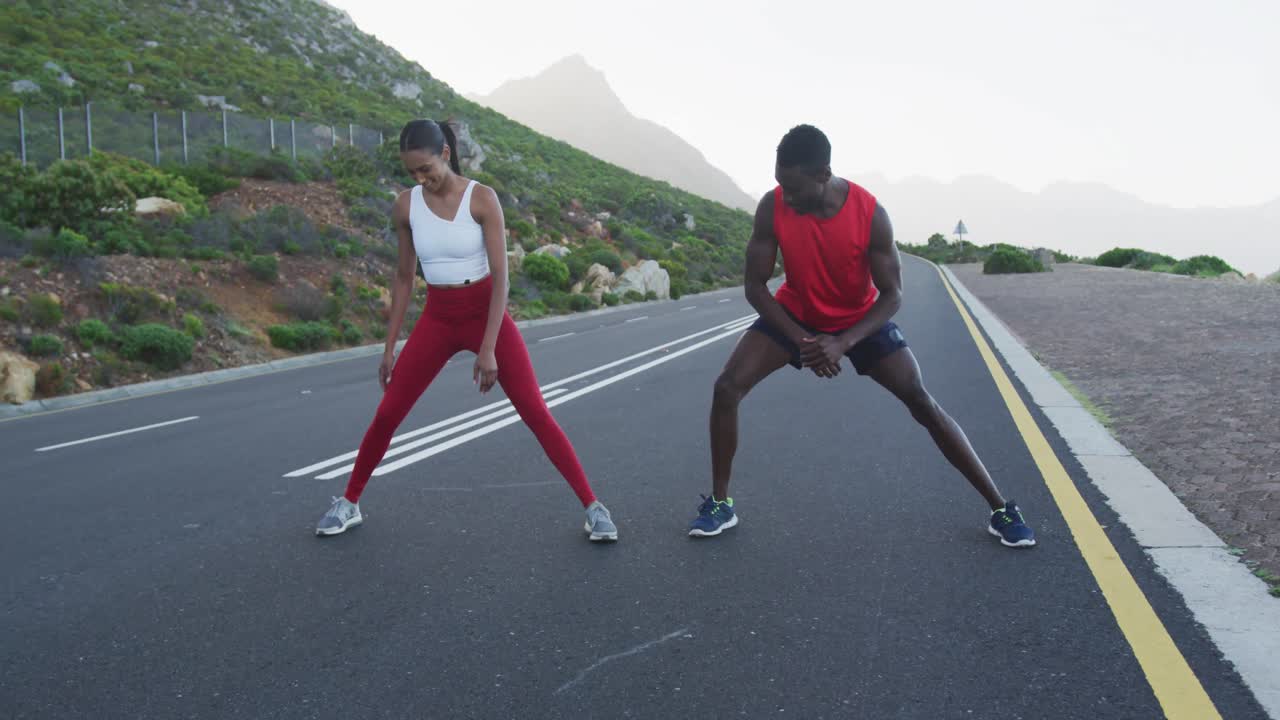 Diverse fit couple exercising stretching on a country road near mountains