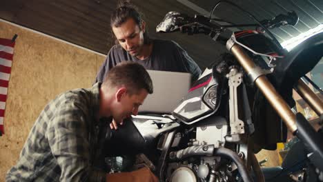 a more experienced mechanic is helping his trainee to properly disassemble moped parts in the workshop. happy mechanics in their garage workshop inspecting and repairing a motorcycle