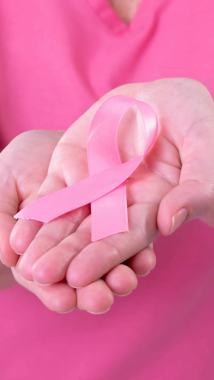 Video del busto di una donna caucasica che tiene in mano un nastro rosa per la consapevolezza del cancro, con sfondo rosa
