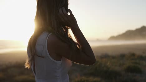 Statische-Zeitlupen-Handaufnahme-Einer-Frau-In-Einem-Weißen-Kleid,-Die-Durch-Ihr-Haar-Streicht-Und-Den-Wunderschönen-Sonnenuntergang-Am-Strand-Beobachtet