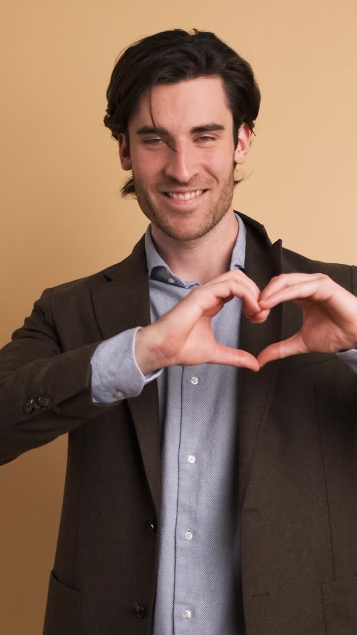 Happy businessman gesturing heart on brown background